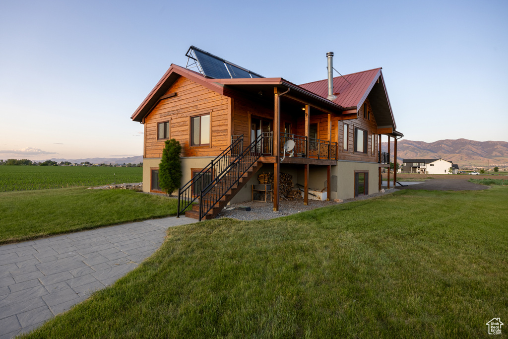 Back of house at dusk with a lawn, stairs, a metal roof, and a mountain view
