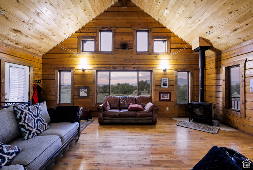 Living area with wooden ceiling, a wood stove, wood finished floors, wooden walls, and high vaulted ceiling
