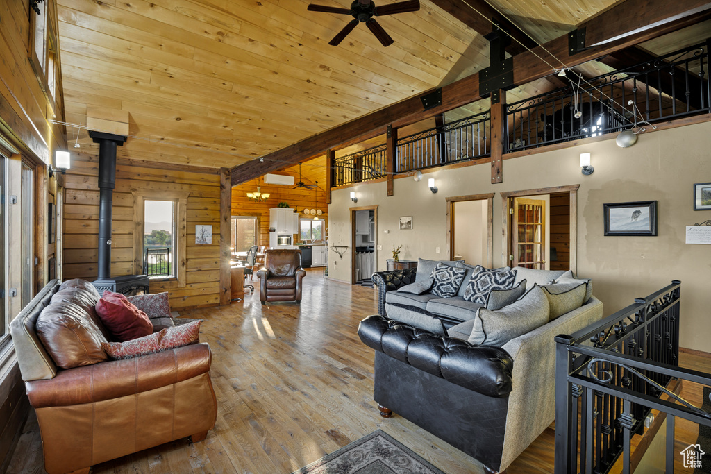 Living area with a wood stove, hardwood / wood-style floors, ceiling fan, wood walls, and high vaulted ceiling
