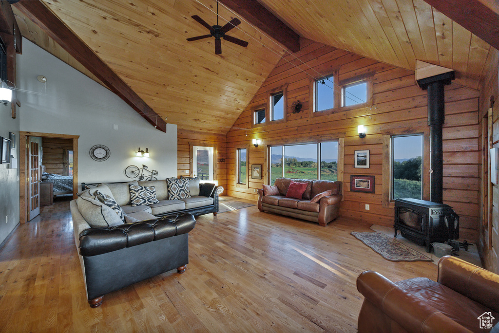 Living room featuring a wood stove, high vaulted ceiling, wood finished floors, ceiling fan, and wooden walls
