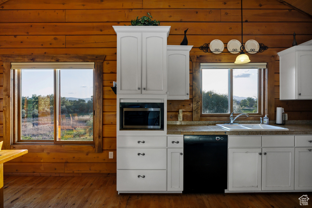 Kitchen featuring black dishwasher, stainless steel microwave, wooden walls, white cabinetry, and dark wood-style floors