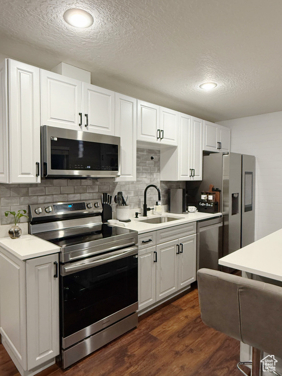 Kitchen featuring stainless steel appliances, dark wood-type flooring, light countertops, white cabinetry, and decorative backsplash