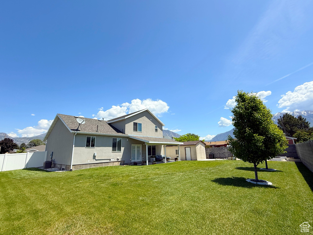 Back of house with a storage unit, a fenced backyard, stucco siding, a shingled roof, and a mountain view
