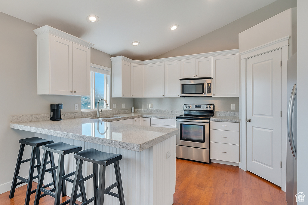 Kitchen with stainless steel appliances, a peninsula, white cabinetry, a breakfast bar, and vaulted ceiling