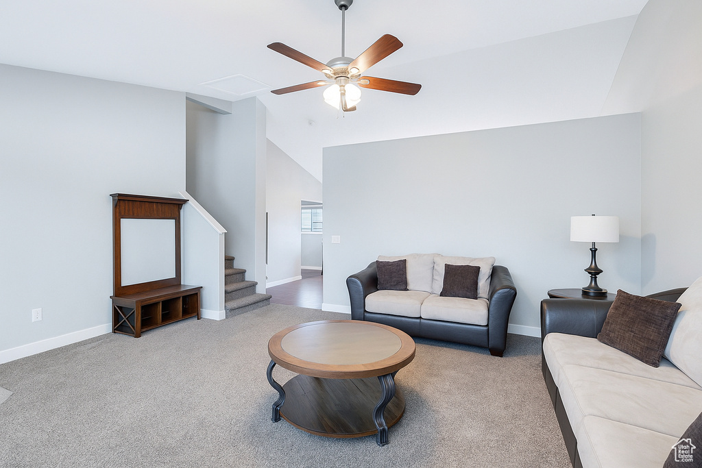 Carpeted living area with ceiling fan, vaulted ceiling, and stairs