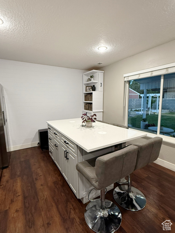 Kitchen featuring a textured ceiling, a center island, dark wood finished floors, a breakfast bar, and light countertops