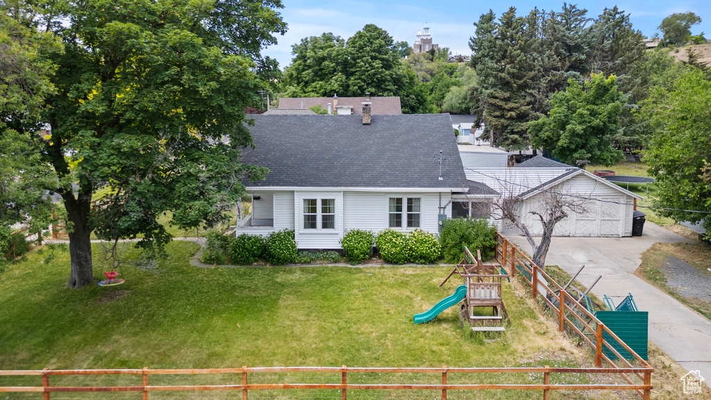 View of front facade with a playground, roof with shingles, concrete driveway, a garage, and a chimney