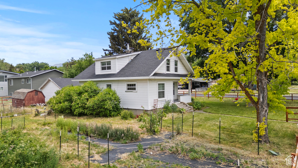 View of side of home with a shingled roof and a storage shed