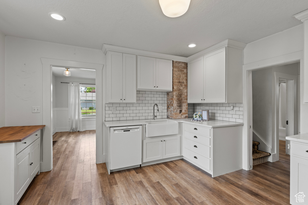 Kitchen with white dishwasher, butcher block counters, white cabinetry, a wainscoted wall, and recessed lighting