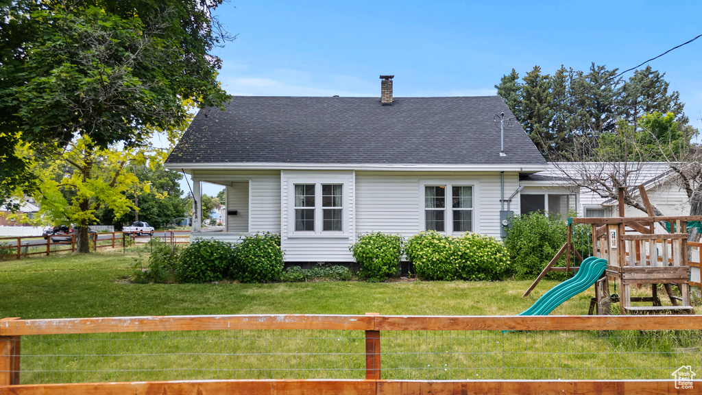 Back of property with a playground, a chimney, and a shingled roof