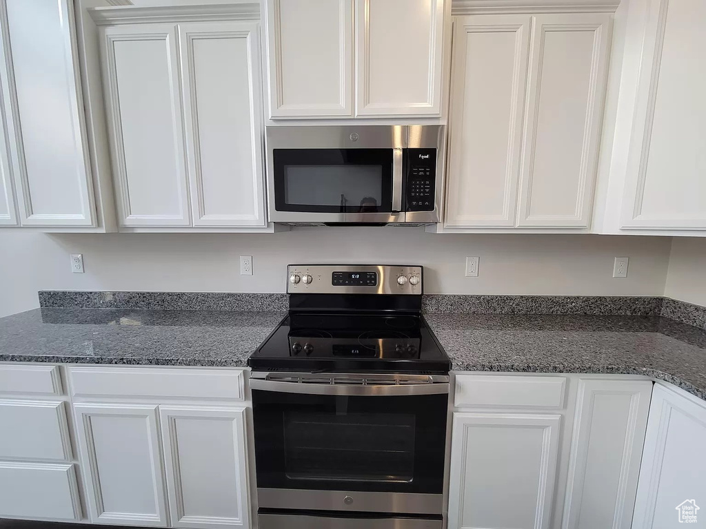 Kitchen with appliances with stainless steel finishes, white cabinetry, and dark stone countertops