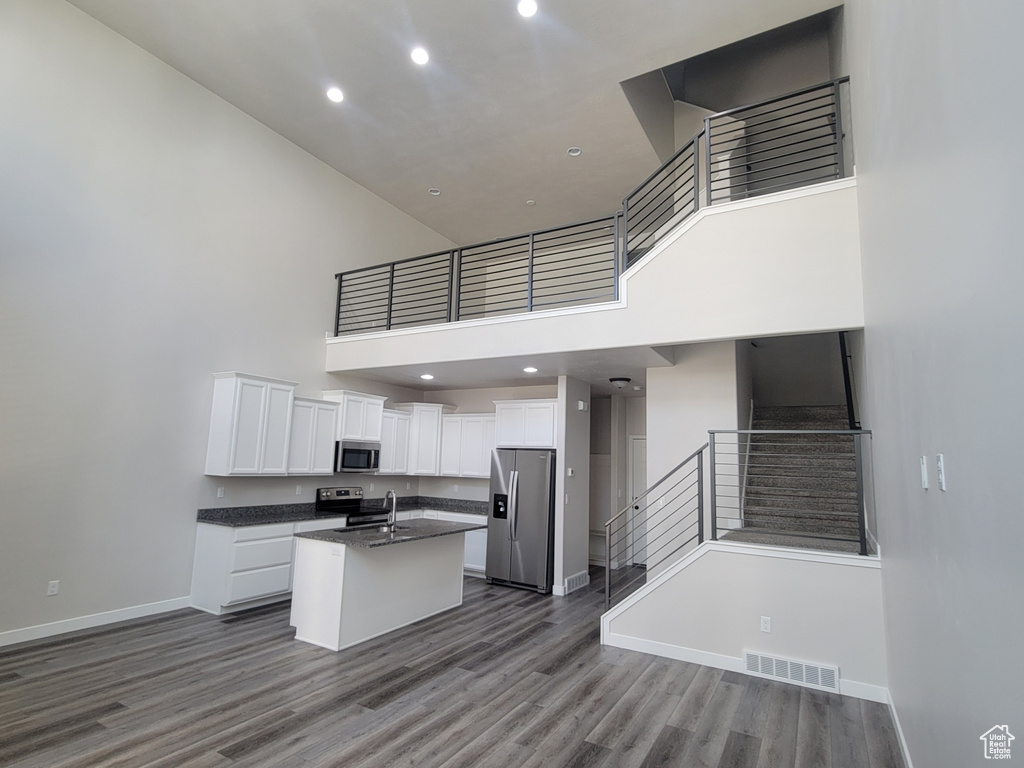 Kitchen with stainless steel appliances, a towering ceiling, dark countertops, white cabinets, and dark wood-type flooring