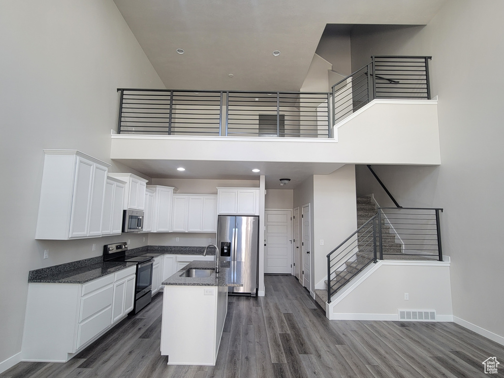 Kitchen with stainless steel appliances, a high ceiling, wood finished floors, white cabinetry, and dark stone counters