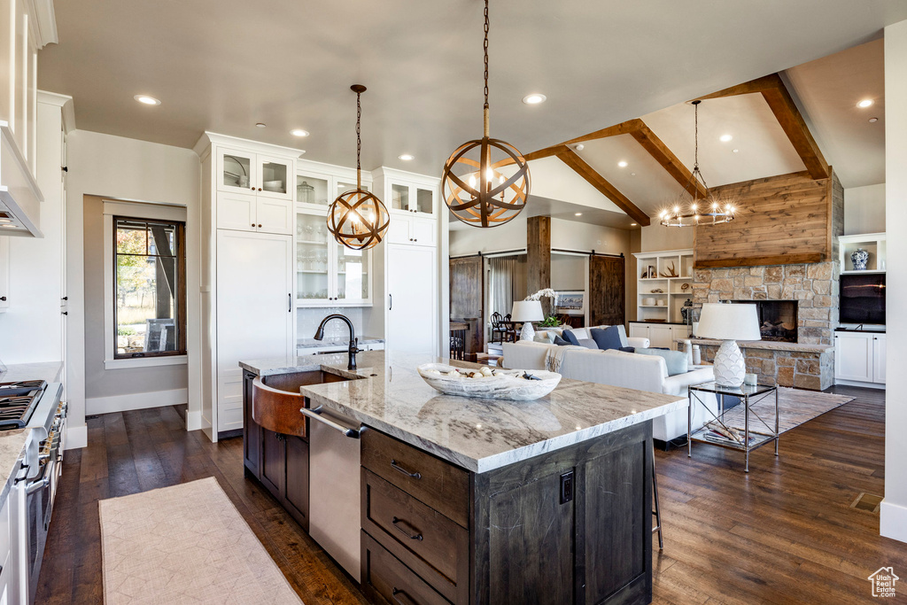 Kitchen with a kitchen island with sink, white cabinetry, appliances with stainless steel finishes, a barn door, and light stone countertops