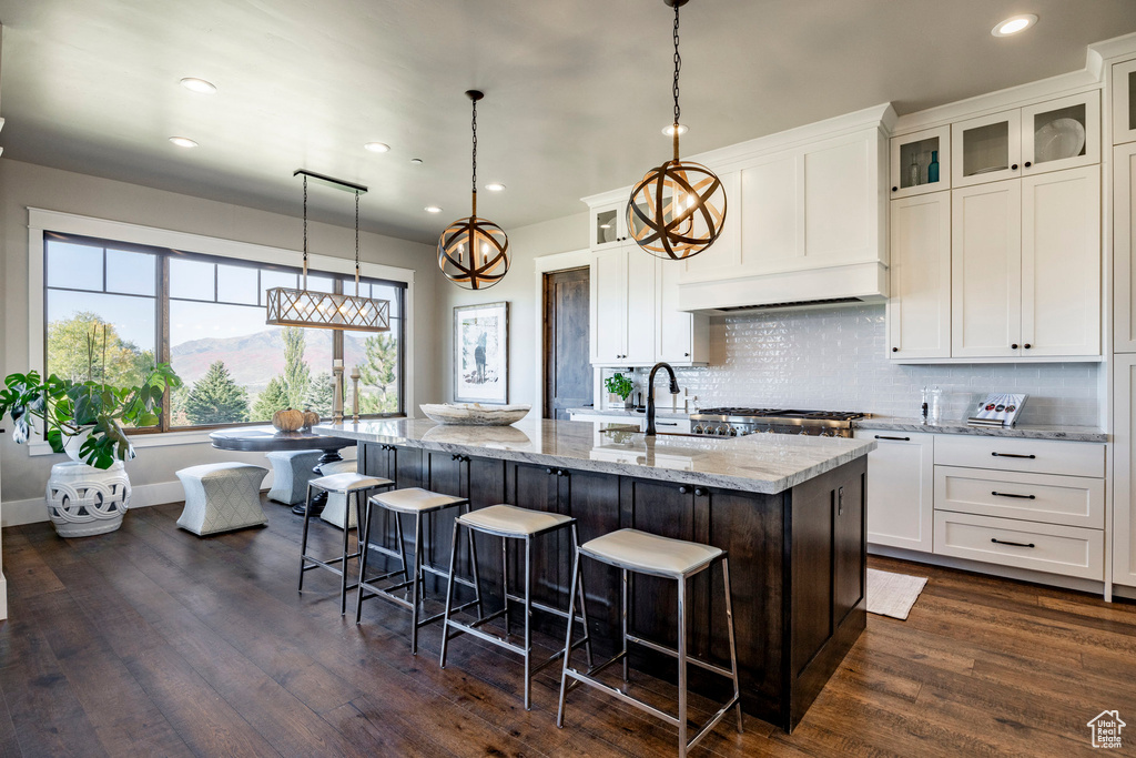 Kitchen with recessed lighting, dark wood finished floors, decorative backsplash, a kitchen island with sink, and light stone countertops
