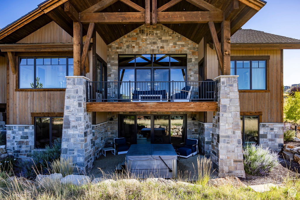 Rear view of property featuring stone siding, a shingled roof, and a balcony