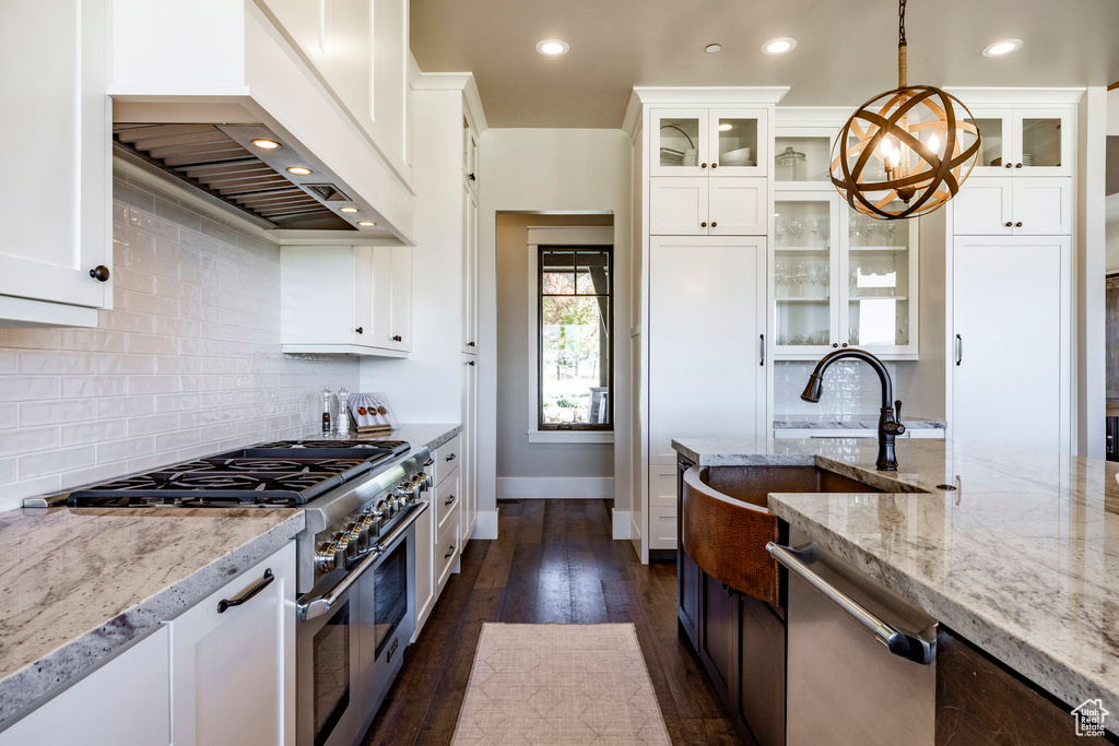Kitchen with stainless steel appliances, custom range hood, light stone countertops, recessed lighting, and hanging light fixtures