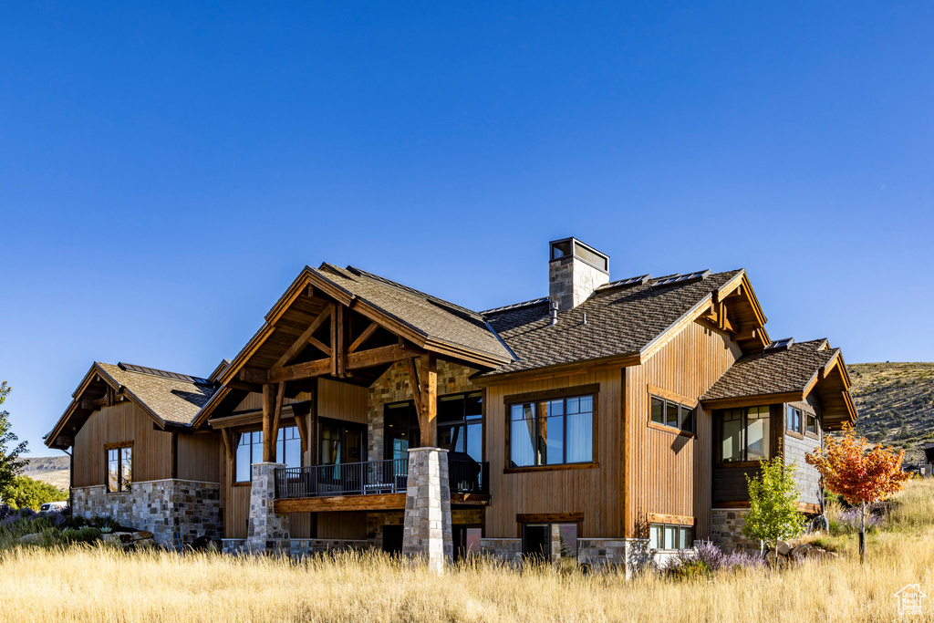 Back of property with stone siding, a chimney, and a shingled roof