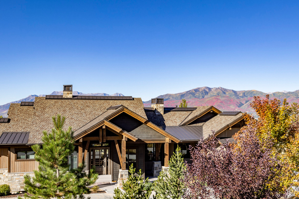 View of front of home with roof mounted solar panels, a chimney, and a mountain view