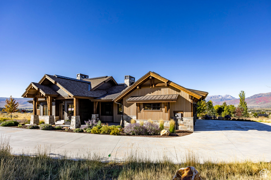 View of front of home with a chimney, concrete driveway, a mountain view, stone siding, and covered porch