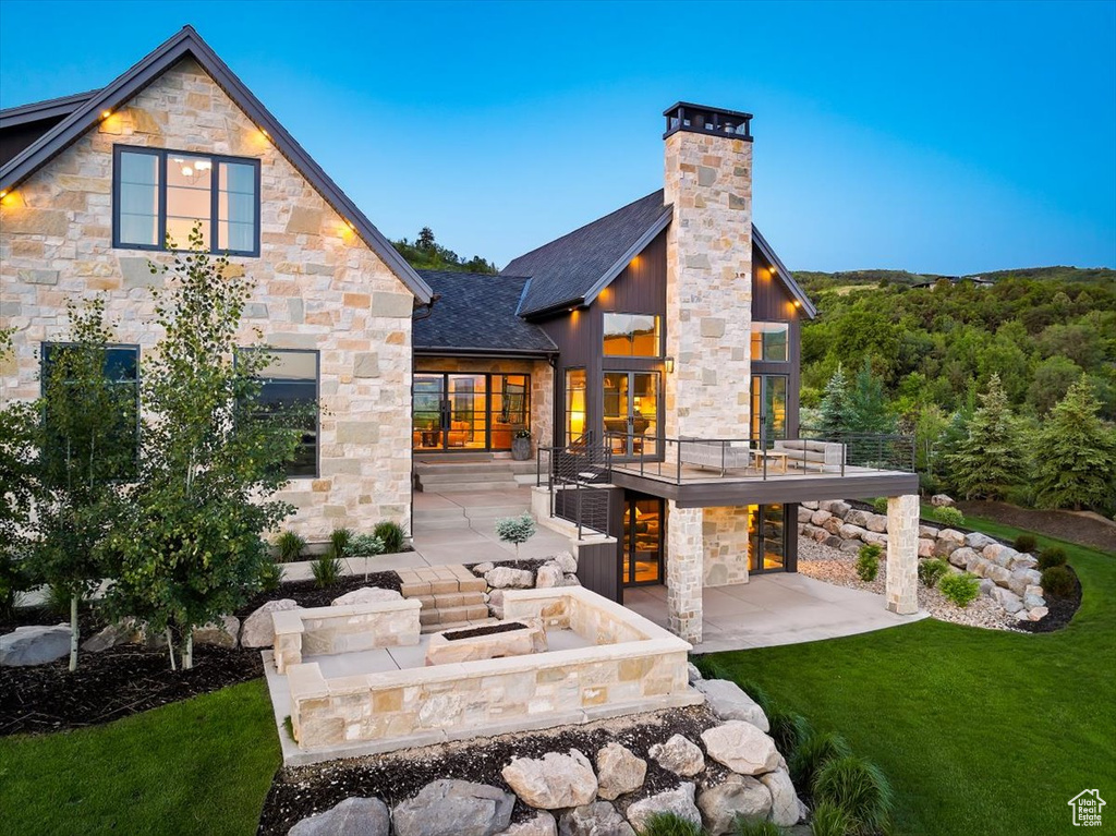 Back of property with stone siding, a patio, a yard, and a chimney