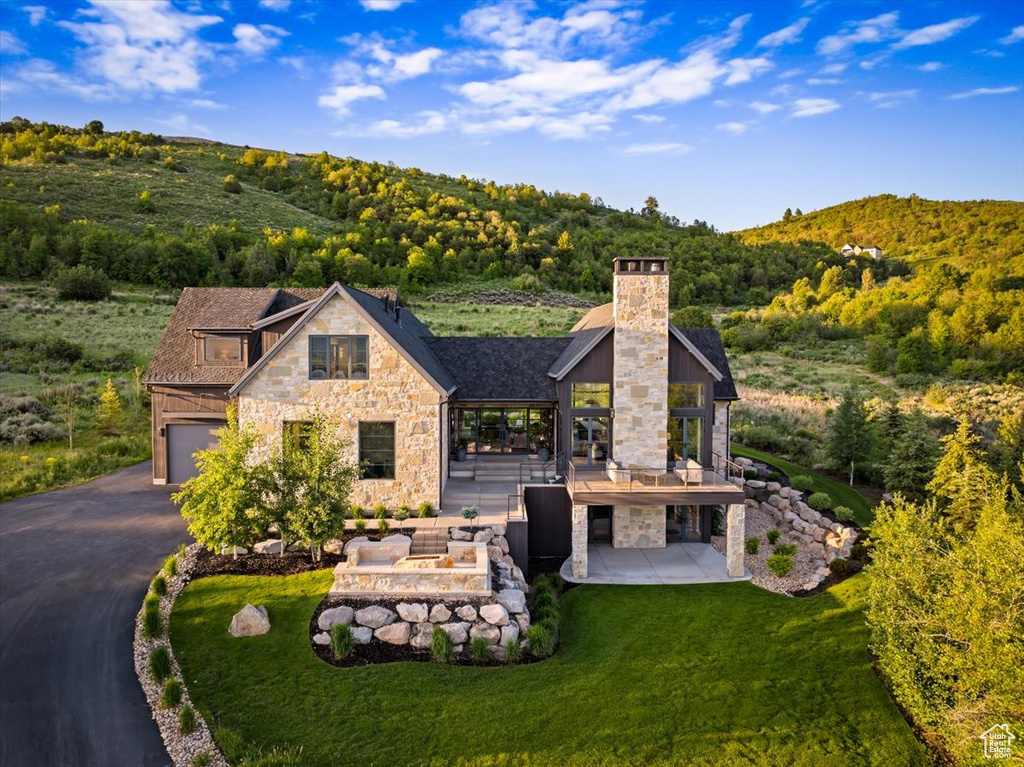 View of front of home with stone siding, a view of trees, driveway, a patio, and a chimney