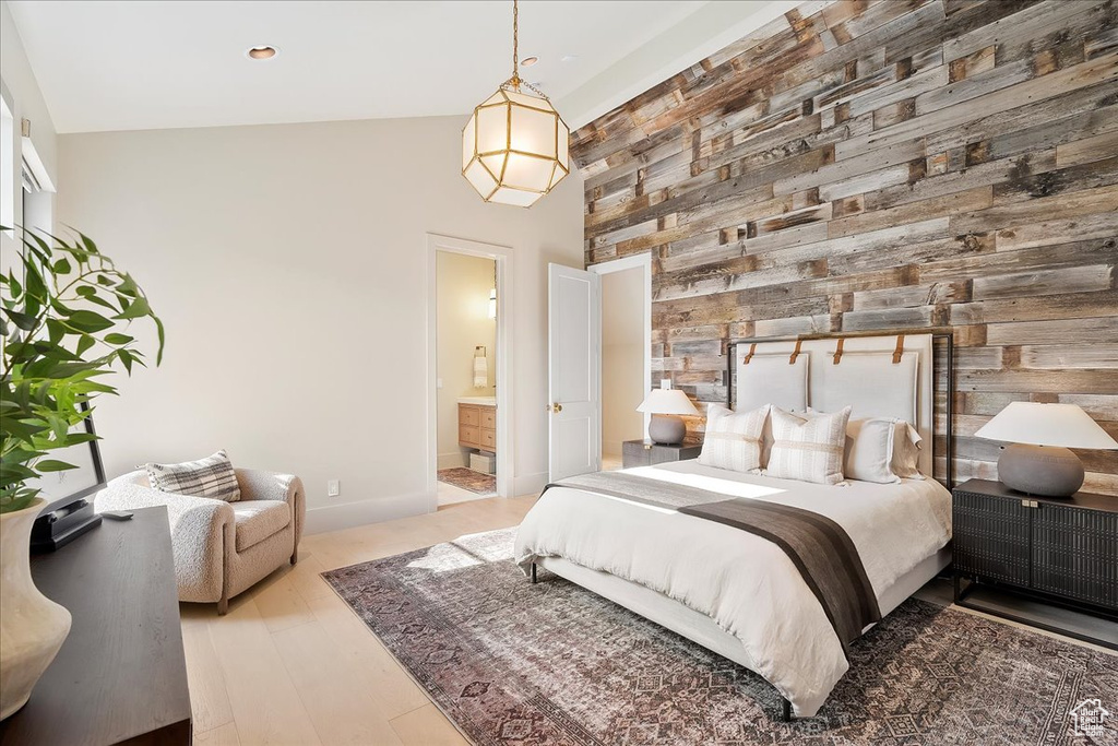 Bedroom featuring wood walls, light wood-style floors, ensuite bathroom, lofted ceiling, and an accent wall
