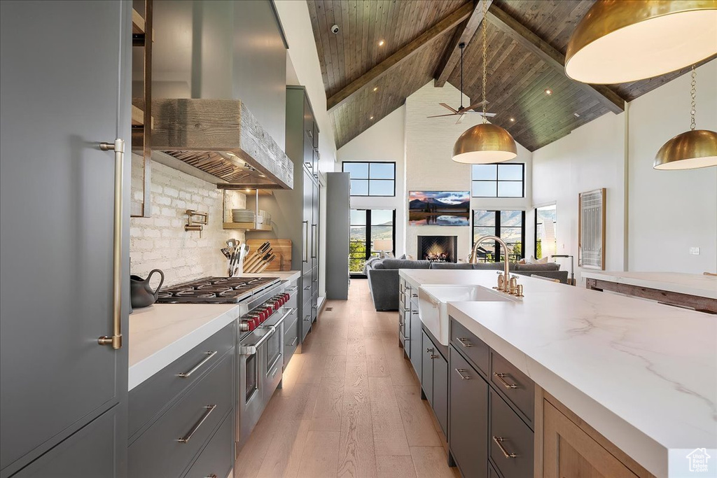 Kitchen with high quality appliances, wall chimney range hood, open floor plan, light wood-style flooring, and high vaulted ceiling