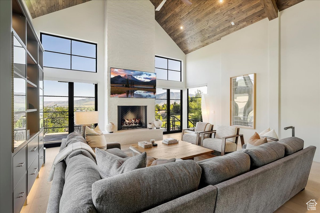 Living area featuring high vaulted ceiling, wood ceiling, a fireplace, light wood-style flooring, and healthy amount of natural light