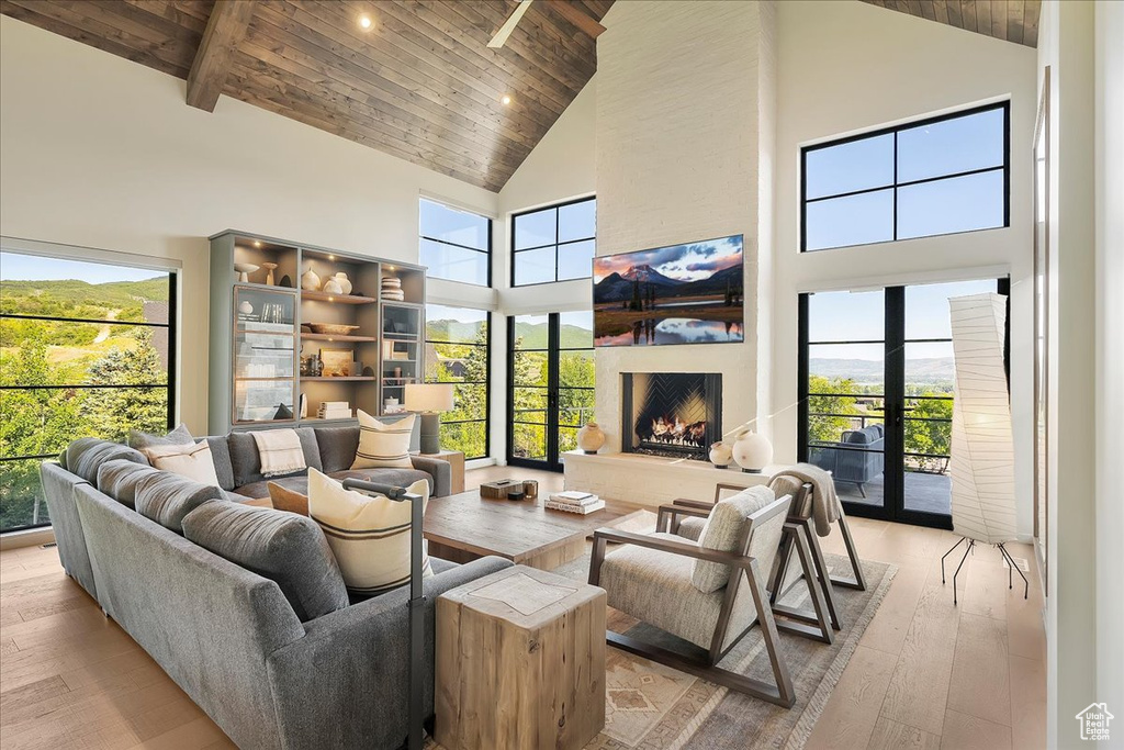 Living room with high vaulted ceiling, a wooden ceiling with exposed beams, light wood-style floors, a fireplace, and plenty of natural light