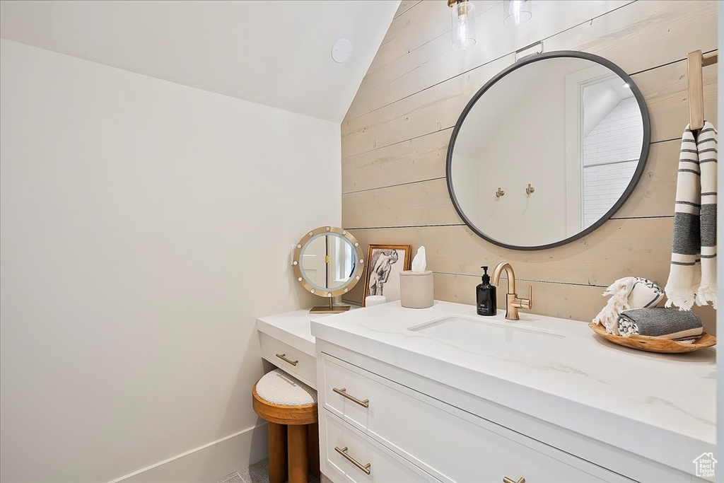 Bathroom with lofted ceiling, vanity, and wood walls