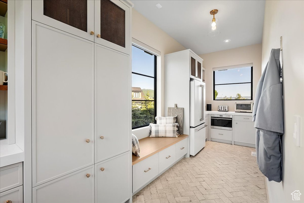 Kitchen featuring high end white fridge, brick patterned flooring, white cabinets, light countertops, and glass insert cabinets