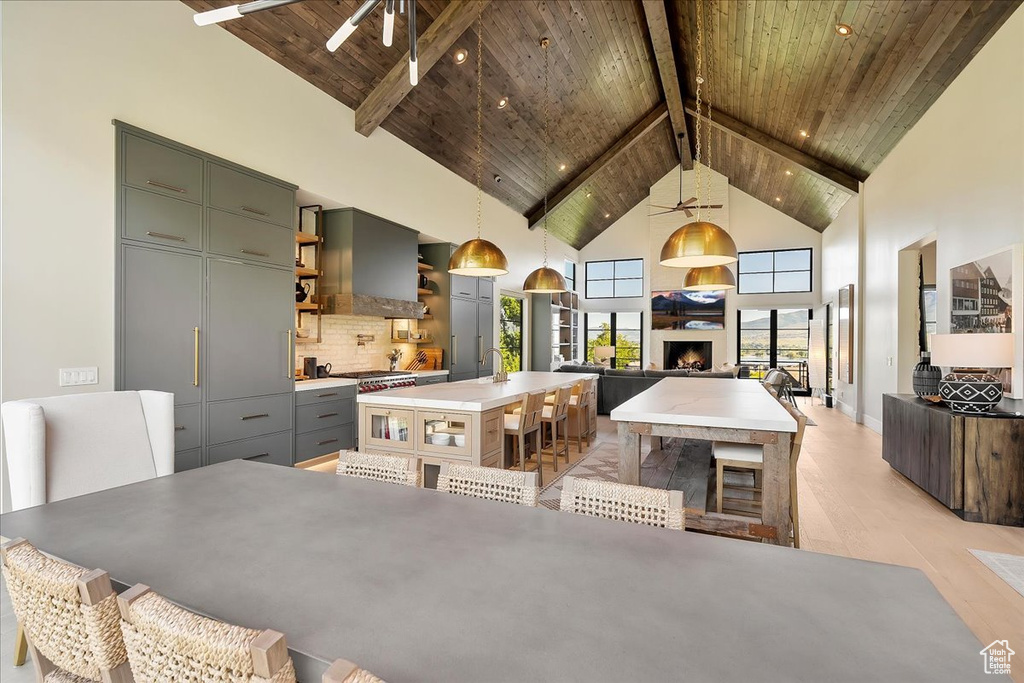 Dining room featuring a wooden ceiling with exposed beams, high vaulted ceiling, light wood-type flooring, a lit fireplace, and a ceiling fan