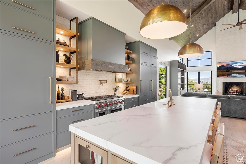 Kitchen with open shelves, wall chimney exhaust hood, gray cabinets, range with two ovens, and high vaulted ceiling