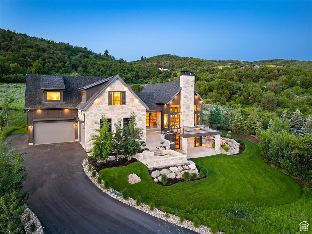 Contemporary house with stone siding, asphalt driveway, a wooded view, and a garage