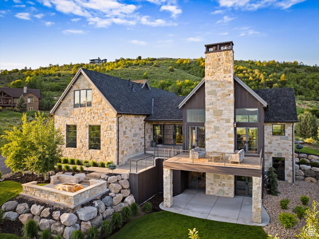 Back of property with stone siding, a chimney, and a patio