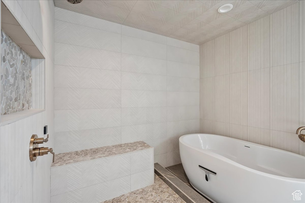 Bathroom featuring a freestanding tub, tiled shower, and tile walls