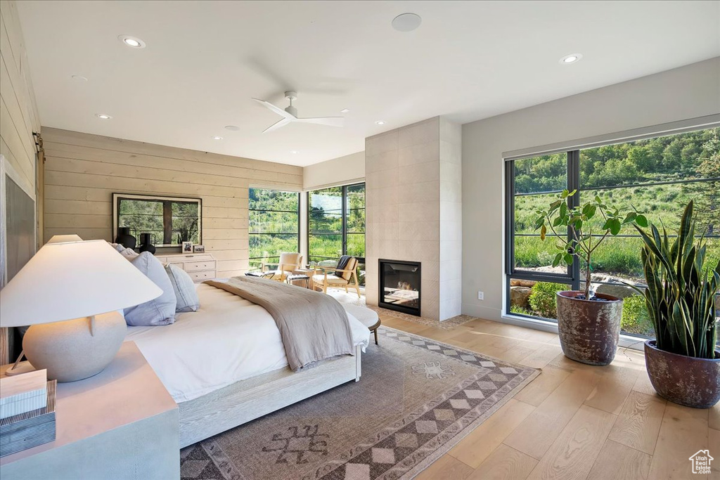 Bedroom with a tiled fireplace, light wood-style floors, recessed lighting, wood walls, and ceiling fan