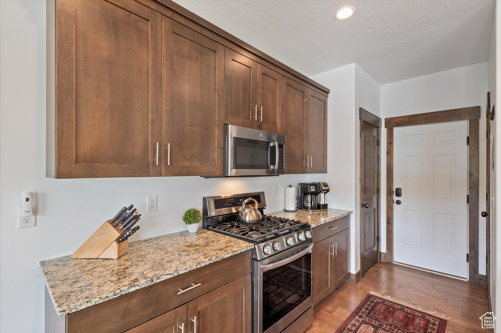 Kitchen with appliances with stainless steel finishes, light wood-style flooring, light stone counters, and recessed lighting