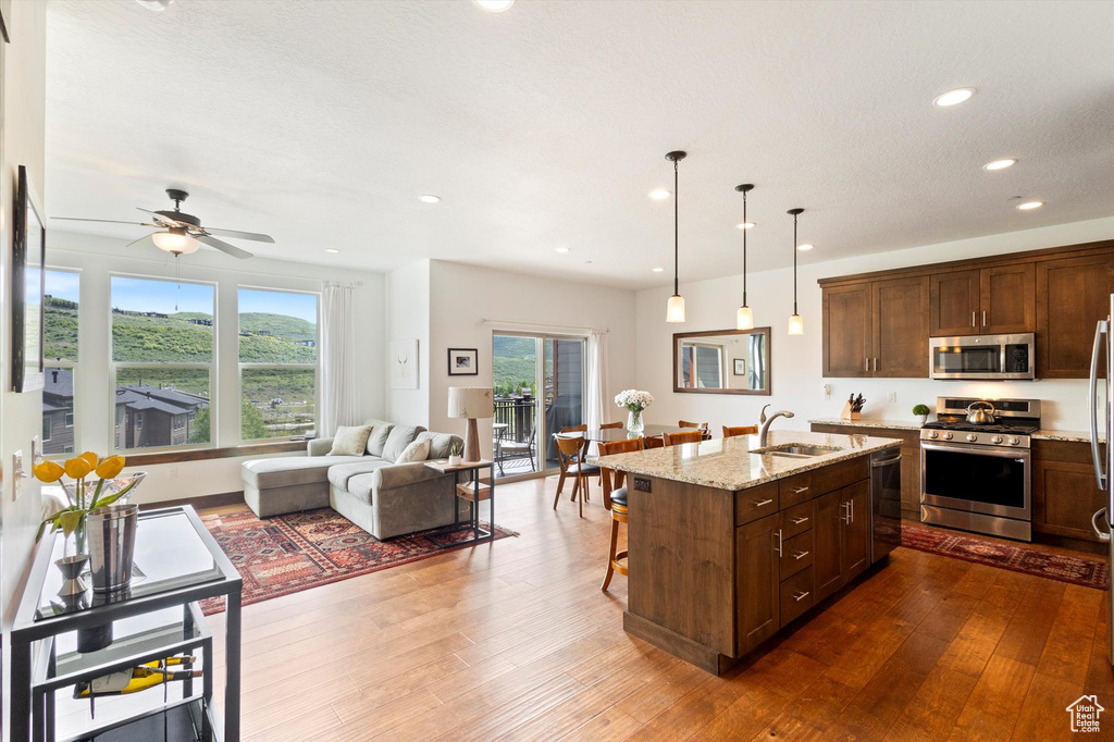 Kitchen featuring stainless steel appliances, open floor plan, light stone counters, a breakfast bar, and dark wood-style floors