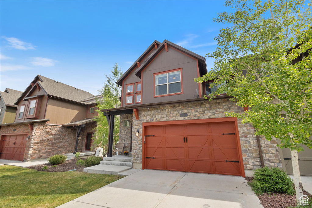 View of front facade featuring stone siding, a garage, and driveway