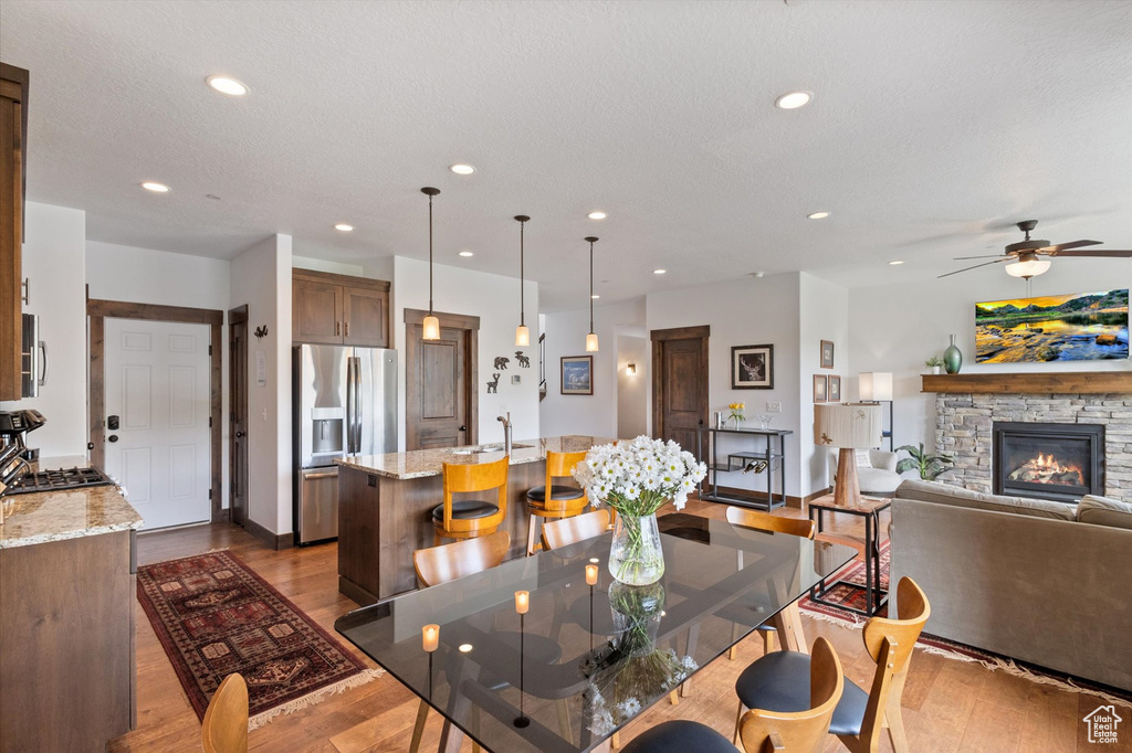 Dining space with a ceiling fan, a fireplace, wood finished floors, and recessed lighting