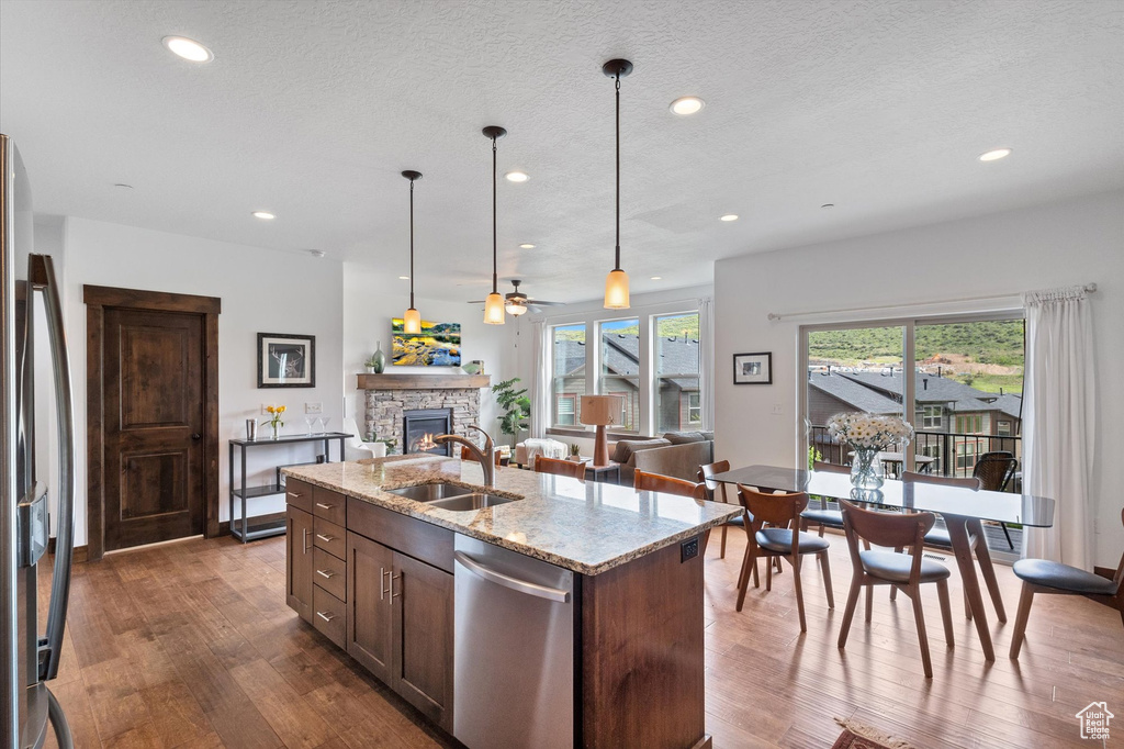 Kitchen with stainless steel dishwasher, a stone fireplace, a ceiling fan, freestanding refrigerator, and dark wood-style flooring