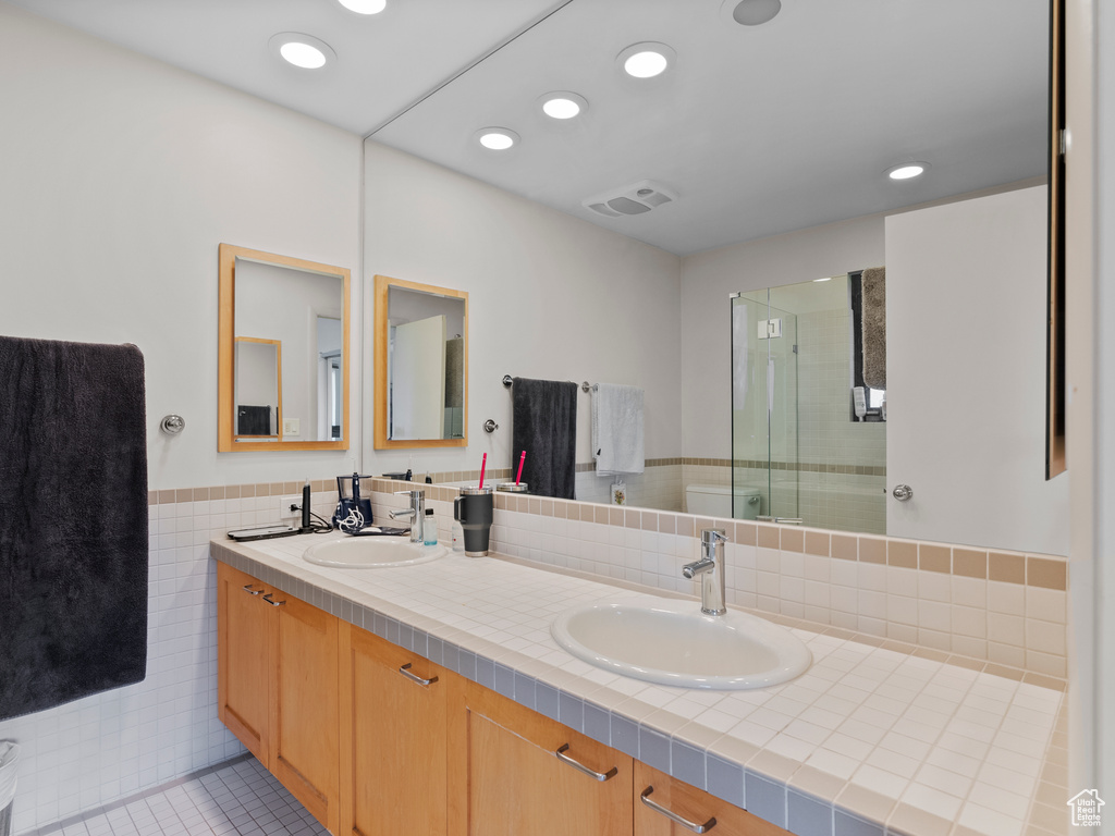 Bathroom featuring double vanity, a shower stall, recessed lighting, tile patterned floors, and a wainscoted wall
