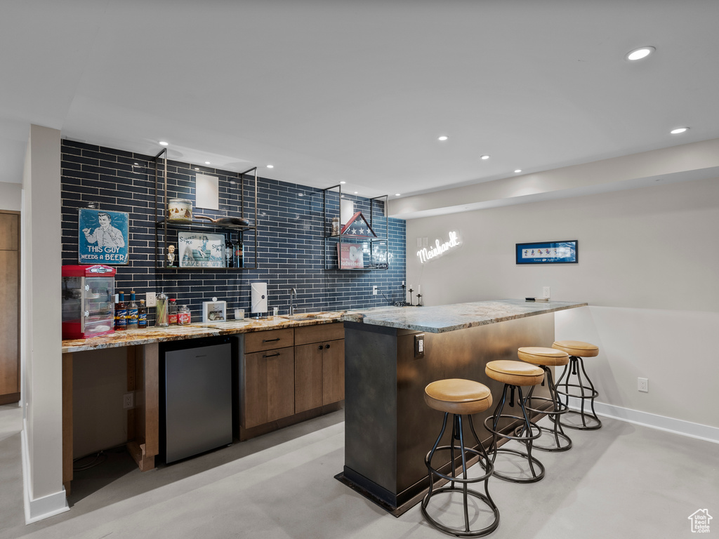 Indoor wet bar with fridge, finished concrete flooring, recessed lighting, and backsplash