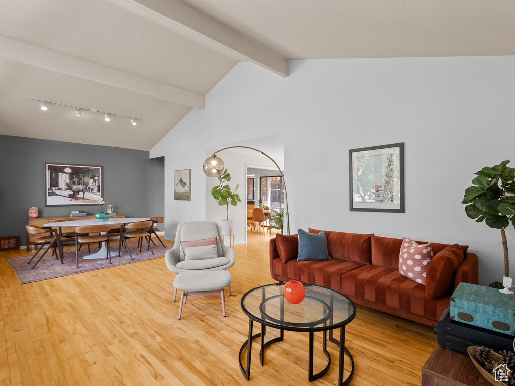Living room with light wood finished floors, beamed ceiling, track lighting, and high vaulted ceiling