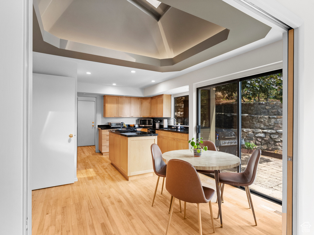 Kitchen featuring light brown cabinets, stainless steel microwave, a kitchen island, dark countertops, and a raised ceiling