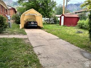 View of green lawn with a storage shed, a detached carport, concrete driveway, and a mountain view