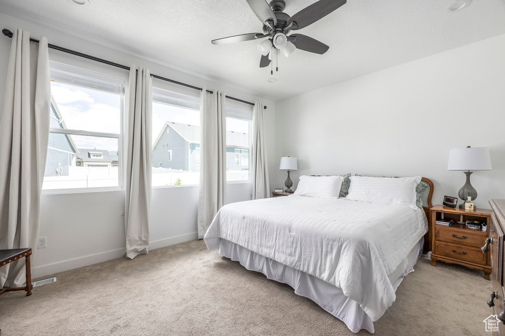 Bedroom with multiple windows, light colored carpet, and a ceiling fan