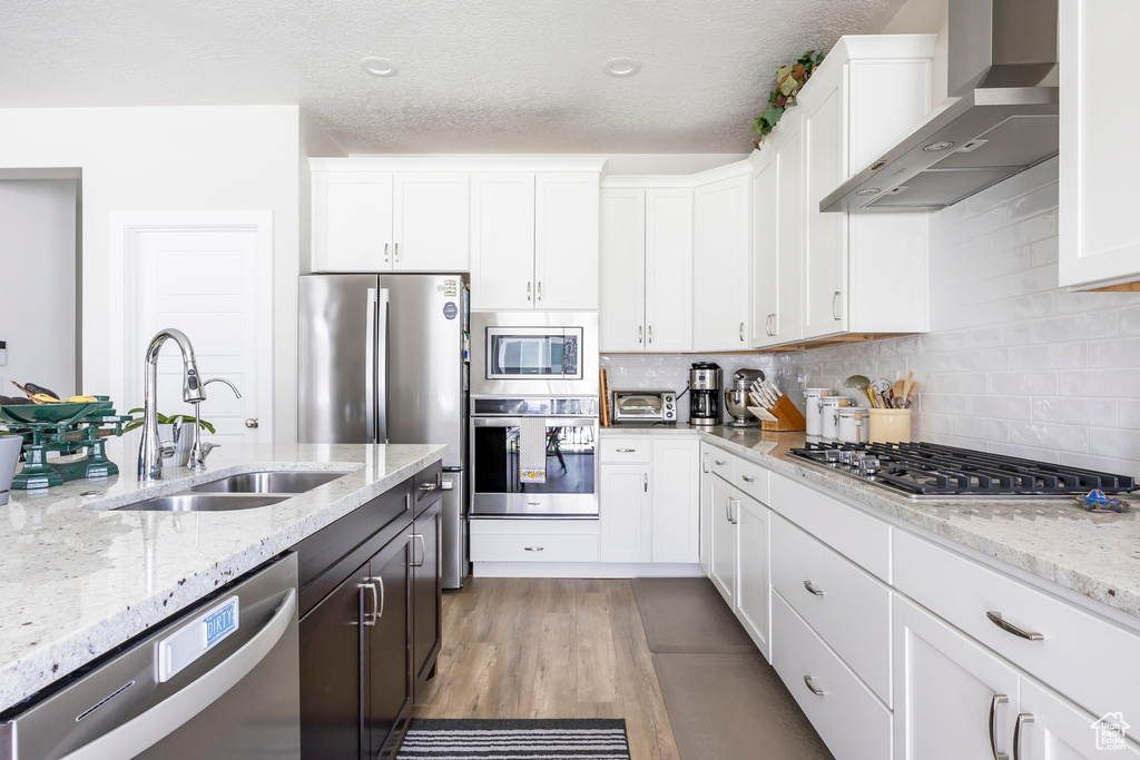 Kitchen featuring wall chimney range hood, stainless steel appliances, white cabinetry, and a textured ceiling